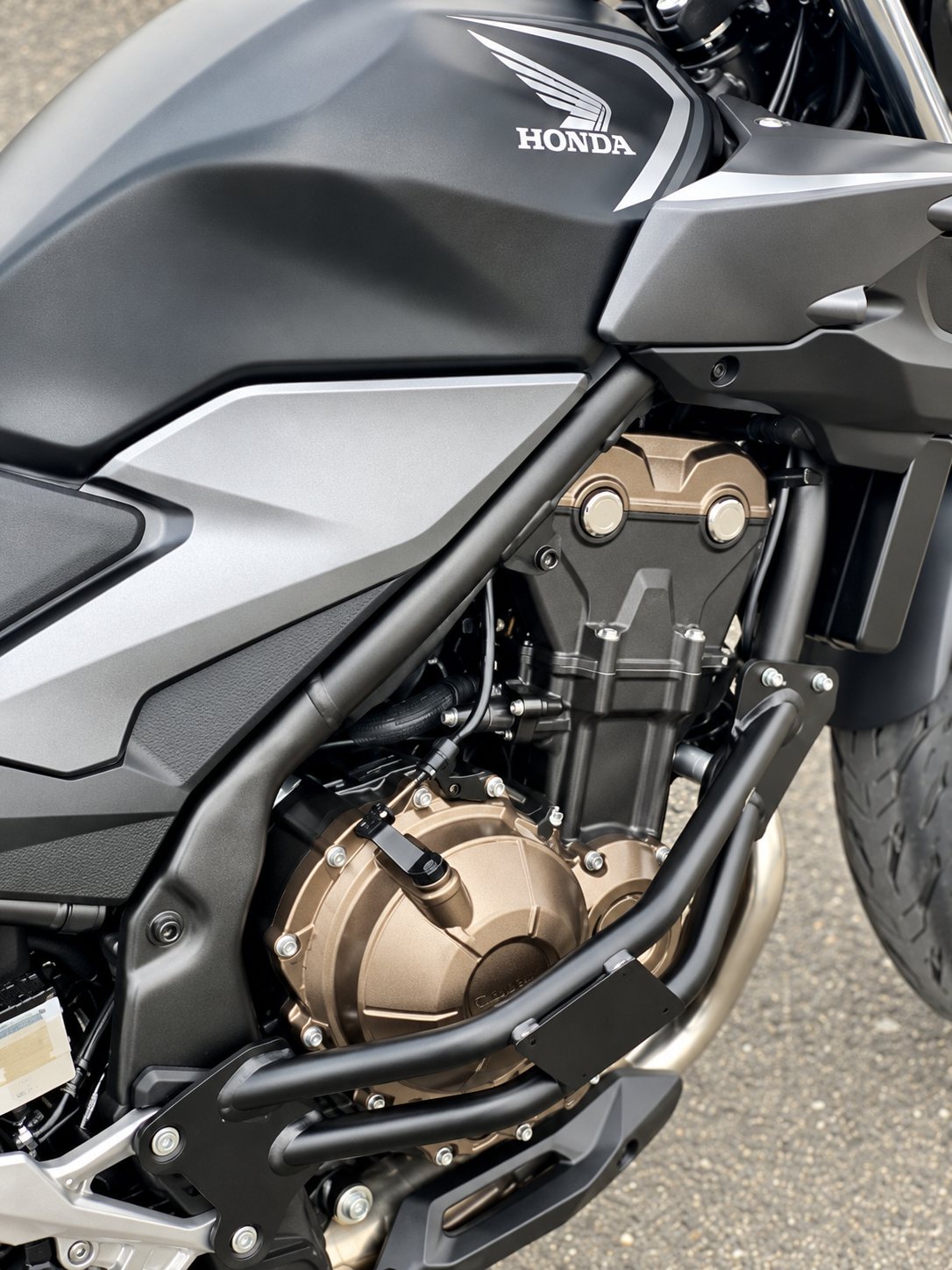 Vue rapprochée du moteur bicylindre cuivré et du cadre noir d'une moto Honda garée sur l'asphalte.
