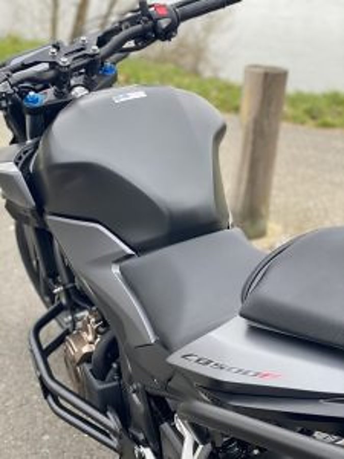 Gros plan sur une moto grise garée près d'un plan d'eau, avec son réservoir, sa selle et son guidon visibles.