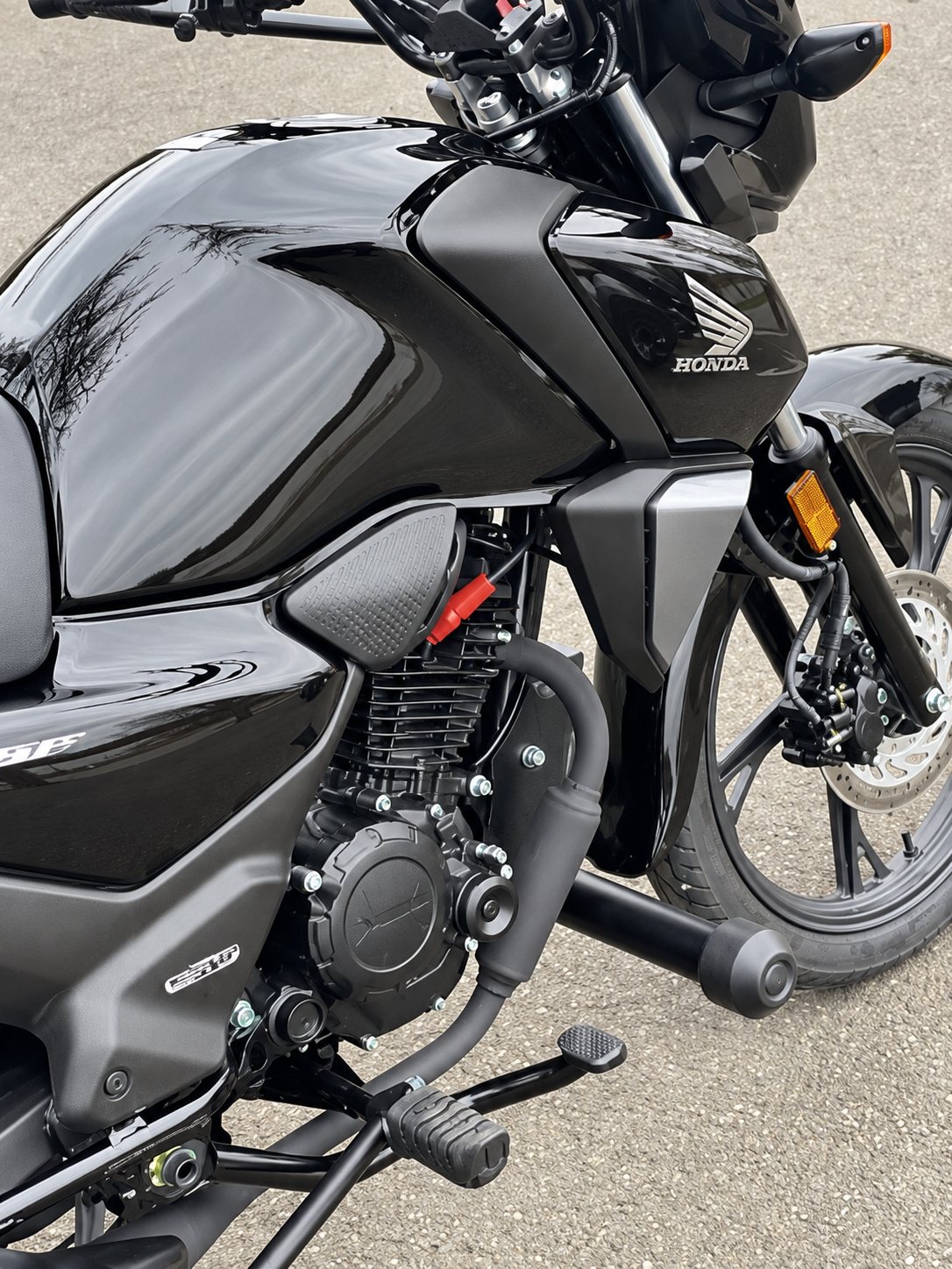 Gros plan sur une moto Honda noire avec son réservoir brillant, son moteur et sa roue avant à disque de frein, garée sur le bitume.