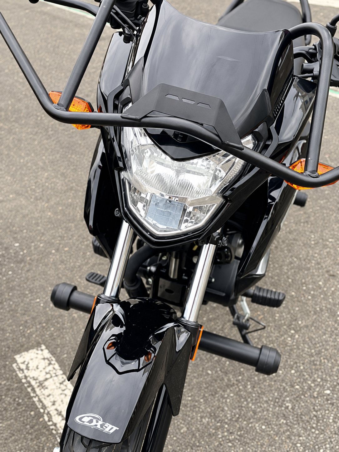 Vue de face d'une moto noire garée sur un parking, avec son phare, son pare-brise et ses arceaux de protection.