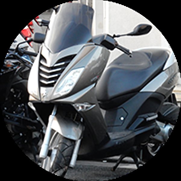 Un scooter gris métallisé équipé d'un grand pare-brise est garé dans la rue, avec d'autres deux-roues et des voitures en arrière-plan.