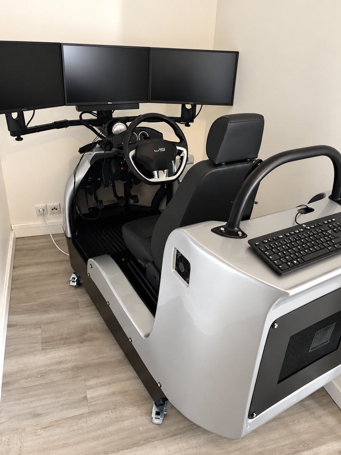 Un simulateur de conduite argenté équipé d'un volant, d'un siège noir, d'un clavier et de trois écrans fixés au mur, installé dans une petite pièce.