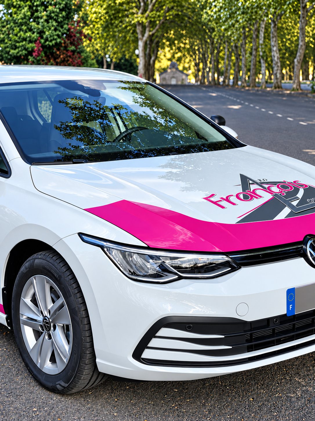Avant d'une voiture blanche aux bandes roses, avec le logo François sur le capot, garée sur une route bordée d'arbres.